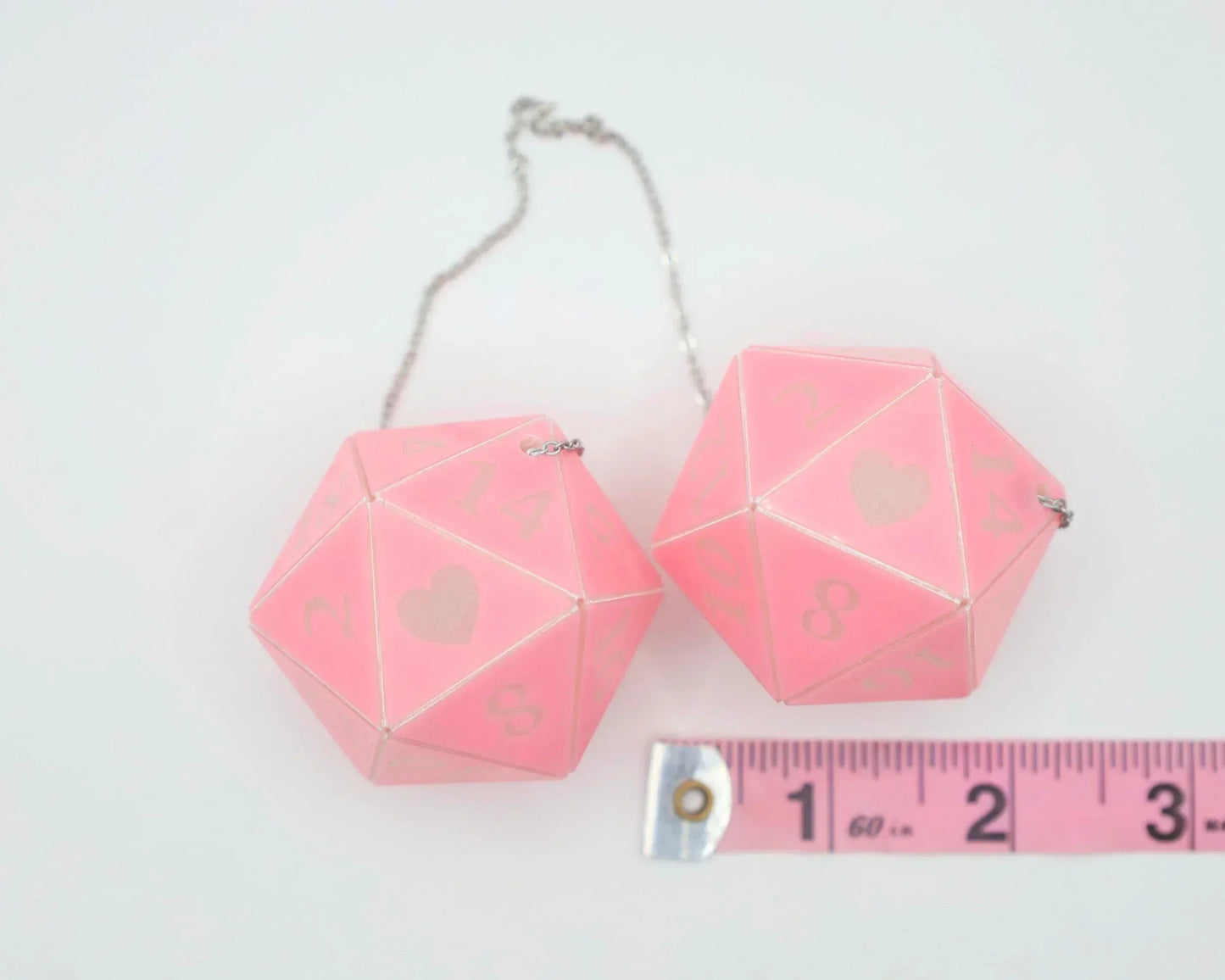 Pink twenty-sided dice car hanging charm with heart design, next to measuring tape