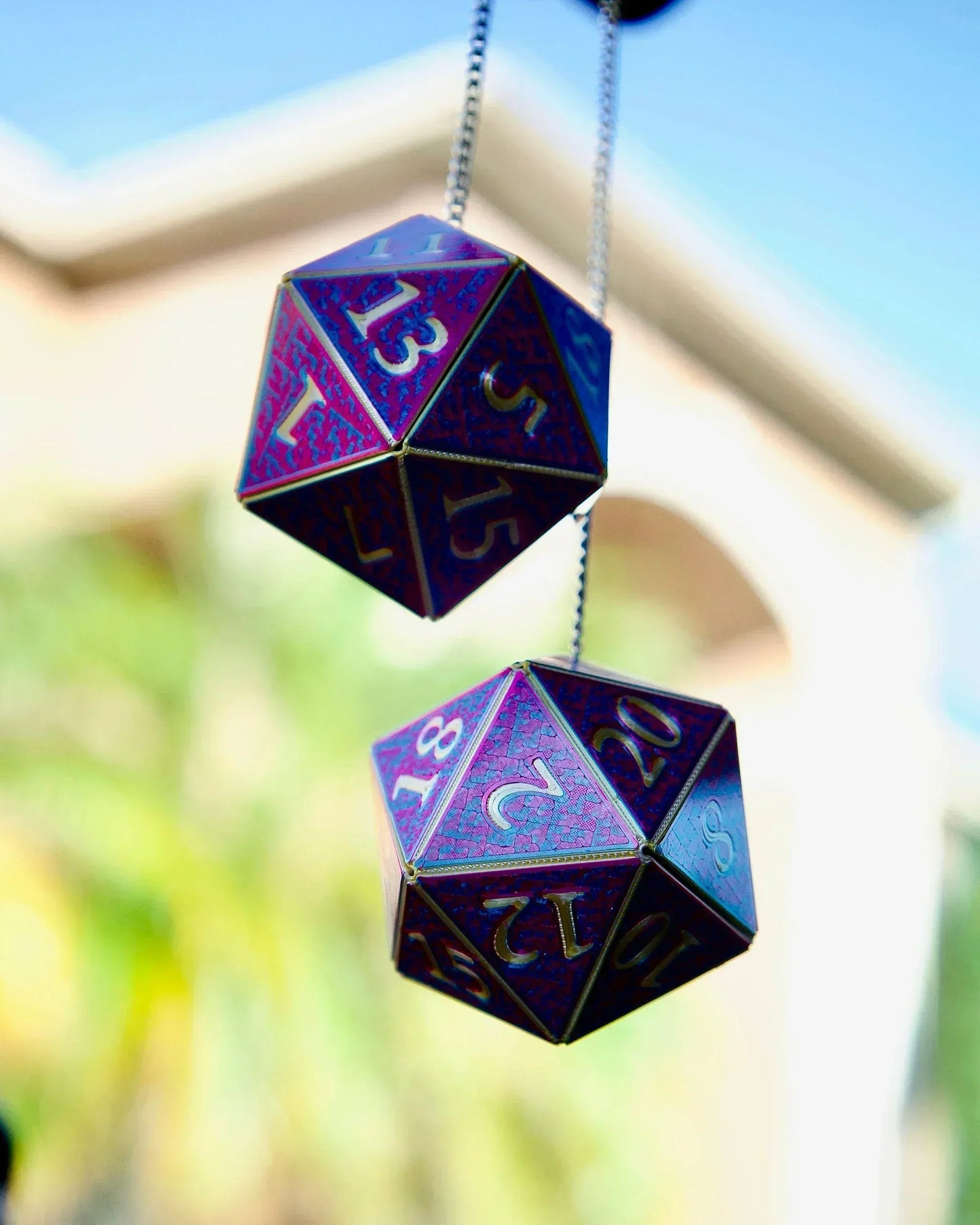 Holographic purple 20-sided dice hanging as car charm with metallic numbers, outdoors.
