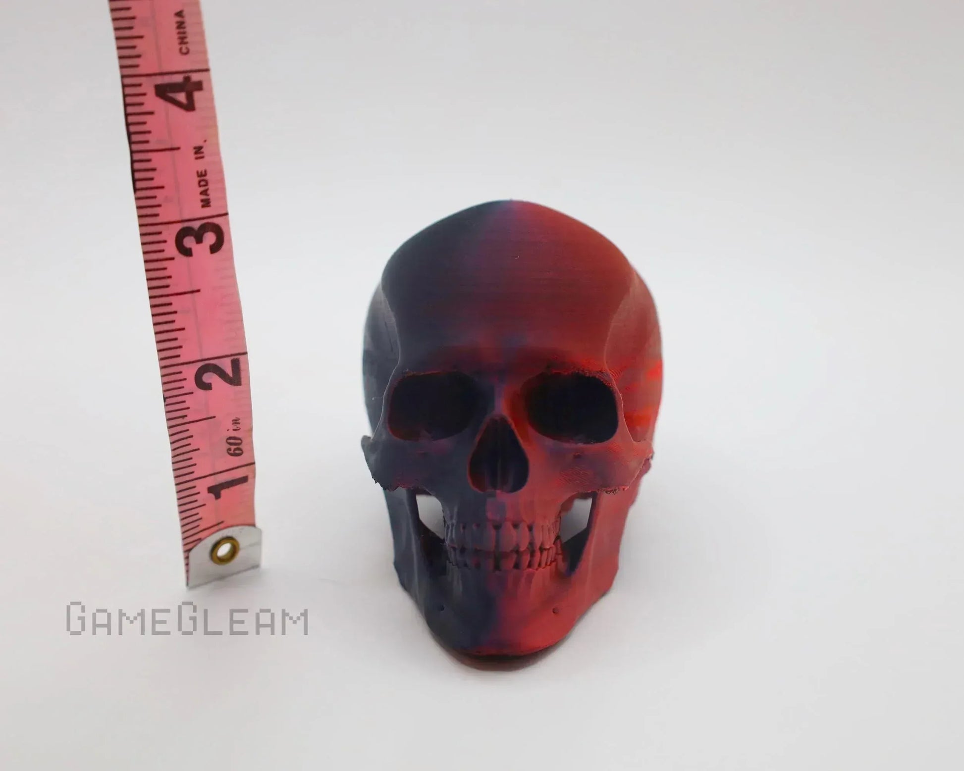 Handmade red and black resin skull decor measured beside a pink tape measure