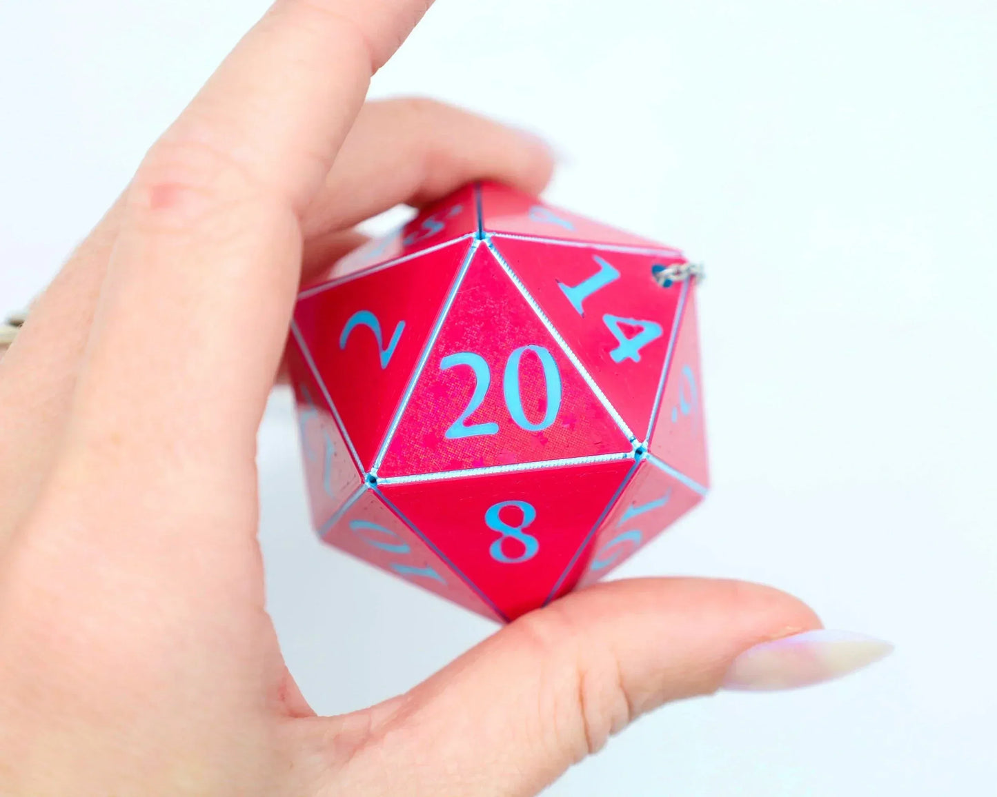 Hand holding a large pink twenty-sided dice charm with blue numbers for tabletop gaming