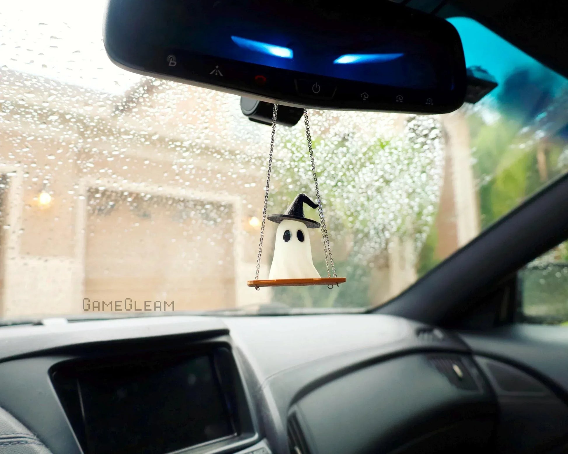 Handmade ghost car charm with wizard hat hanging from rearview mirror on a rainy day