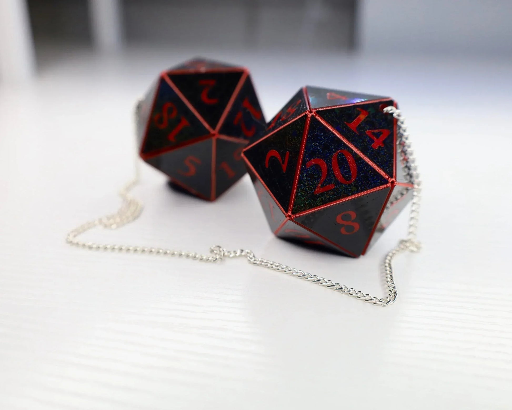 Pair of black and red 20-sided dice car charms with silver chain on white surface