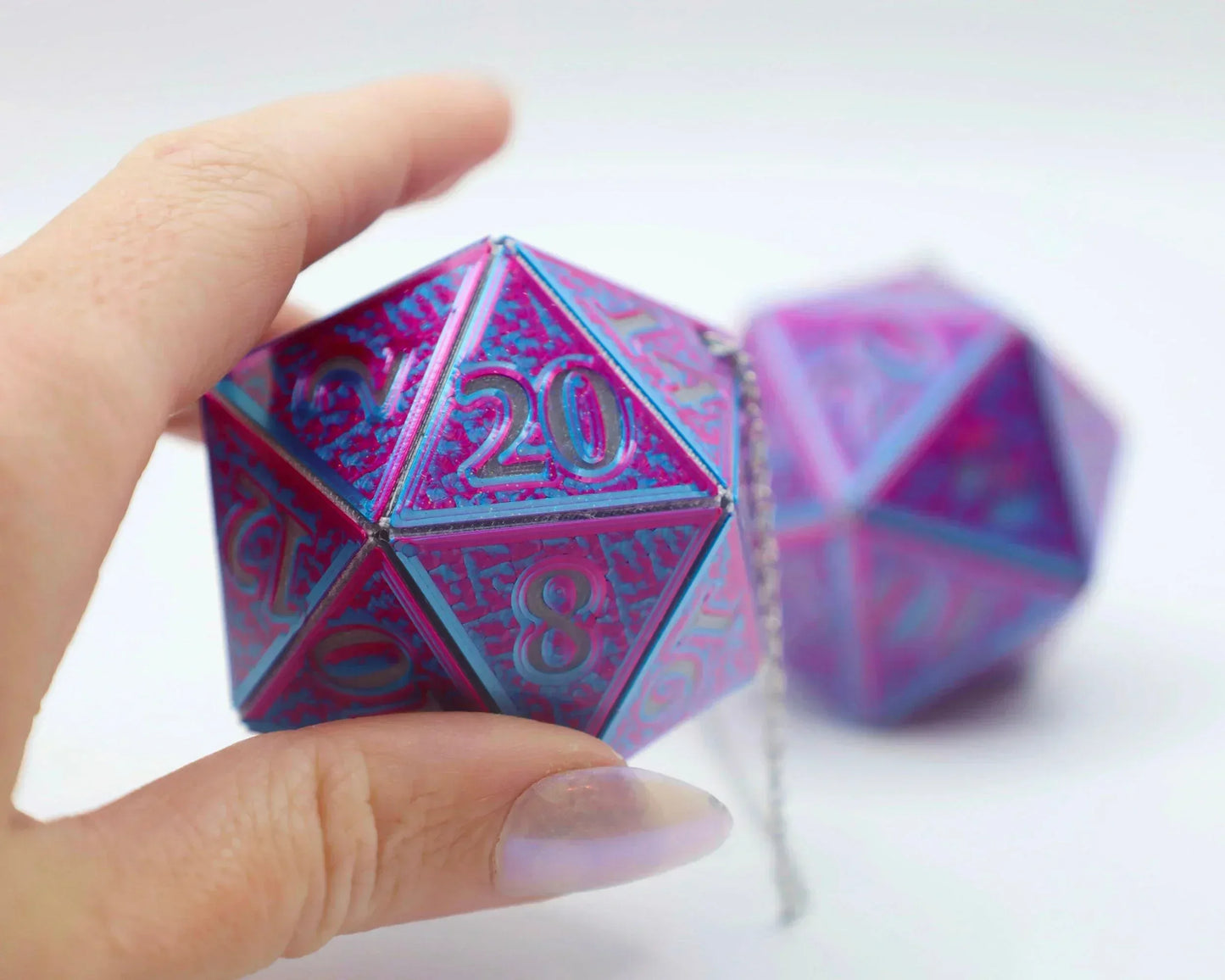 Hand holding holographic car charm shaped like a large pink and blue twenty-sided die.