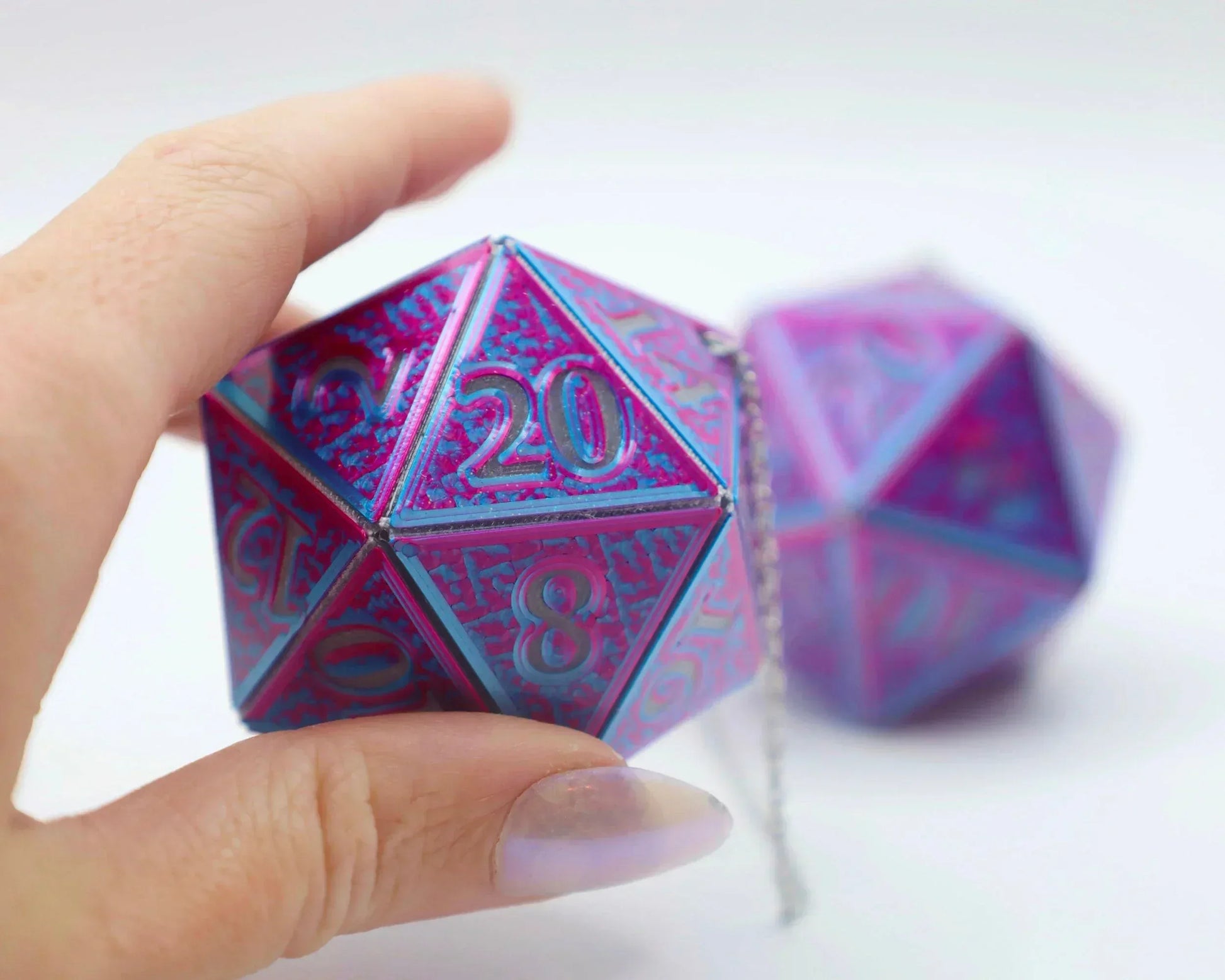 Hand holding holographic car charm shaped like a large pink and blue twenty-sided die.
