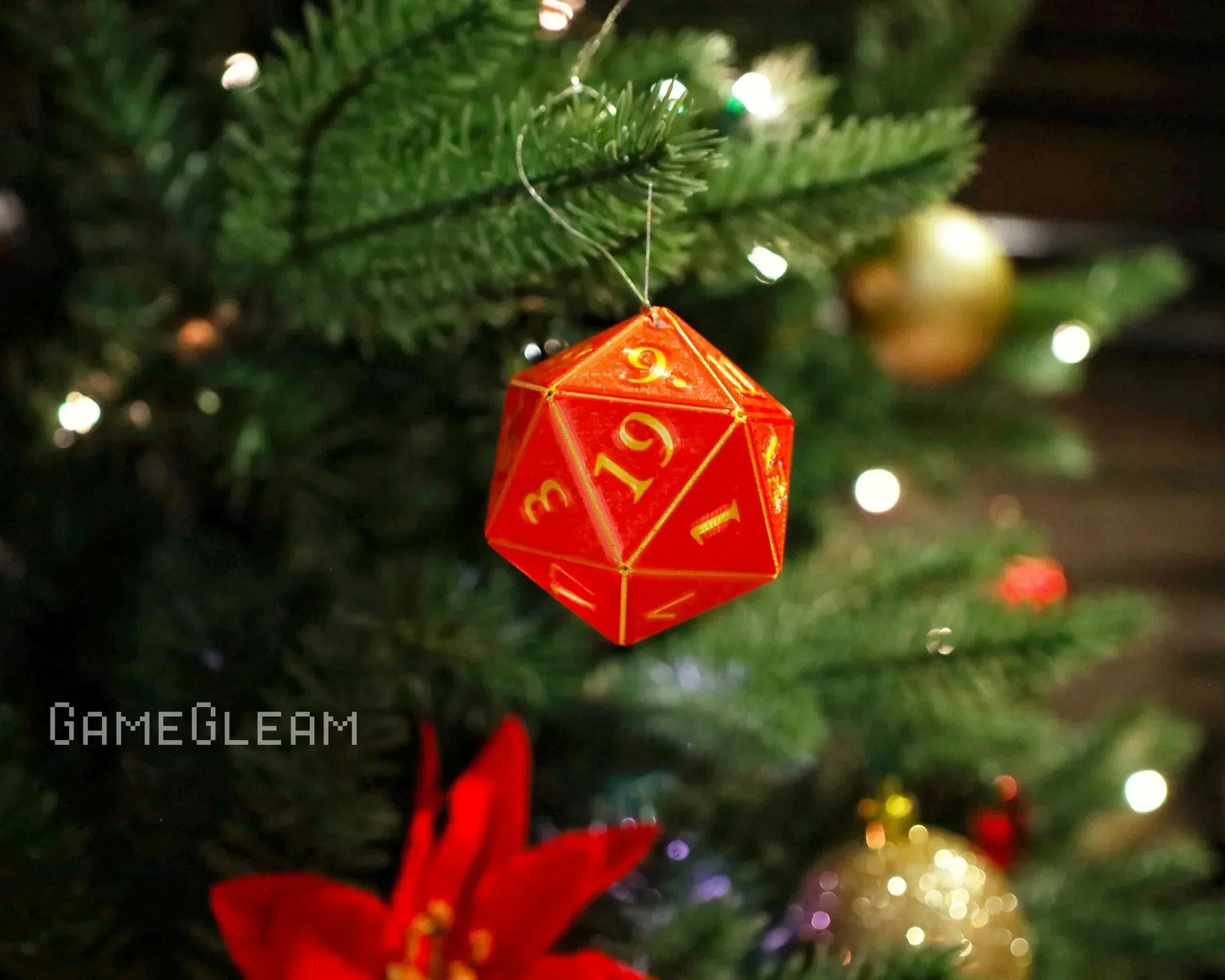 Red twenty-sided dice ornament with gold numbers hanging on a Christmas tree with lights.