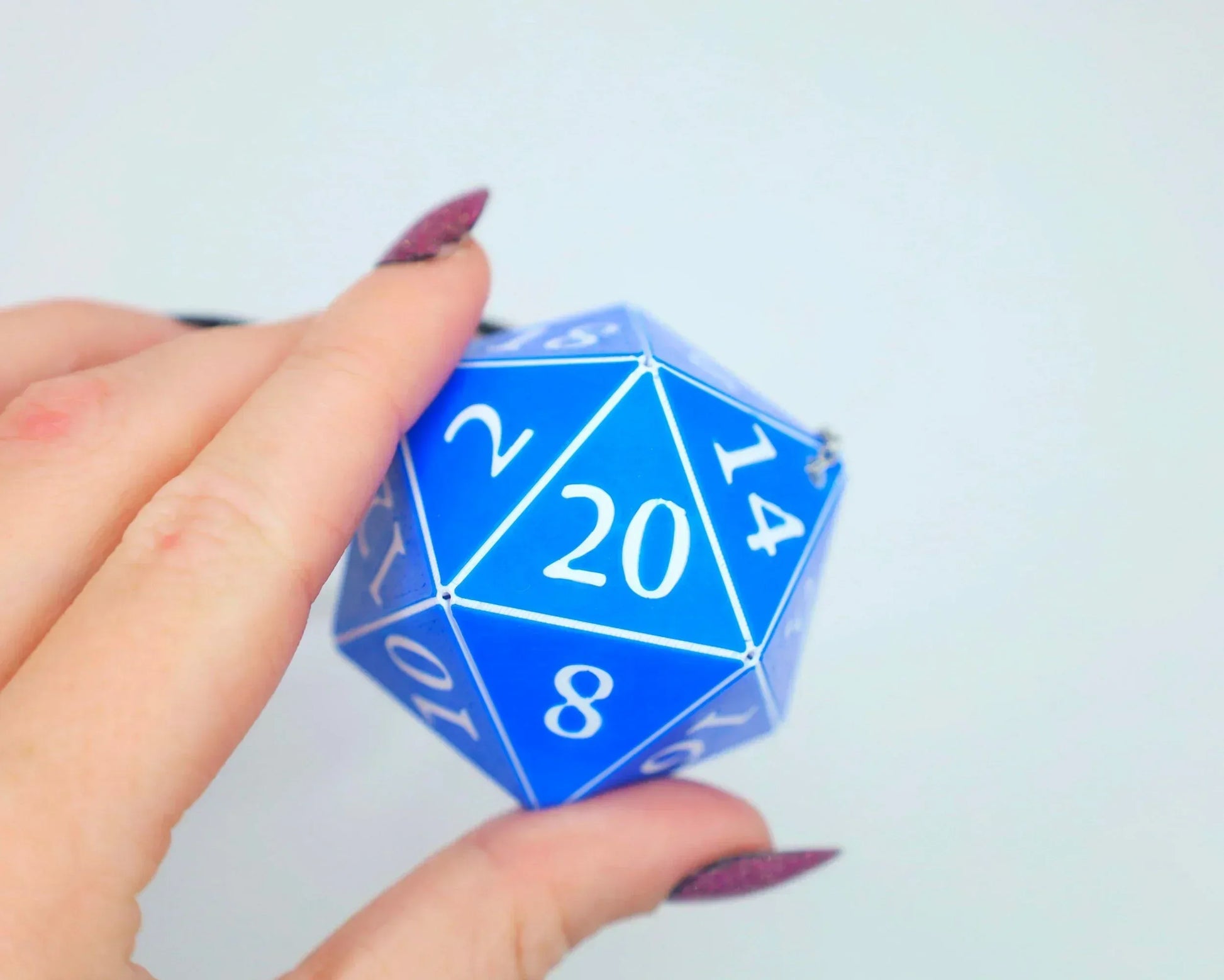 Hand holding a large blue 20-sided dice with white numbers, tabletop gaming accessory
