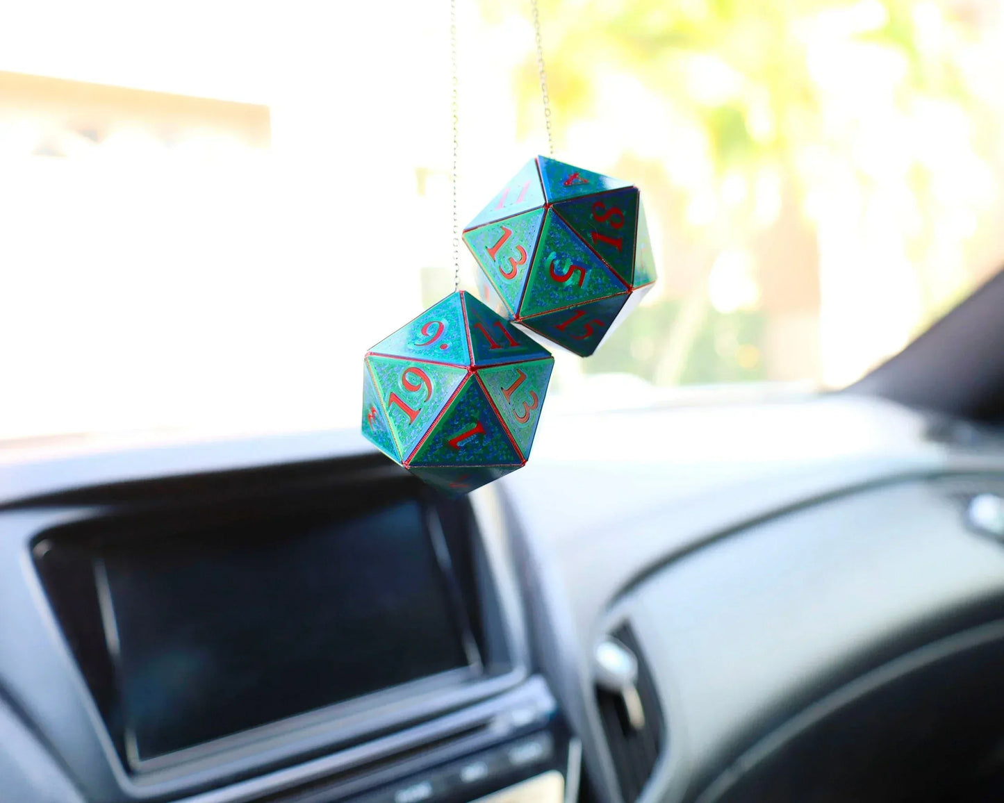 Holographic twenty-sided dice car charm hanging from rearview mirror in vehicle interior.