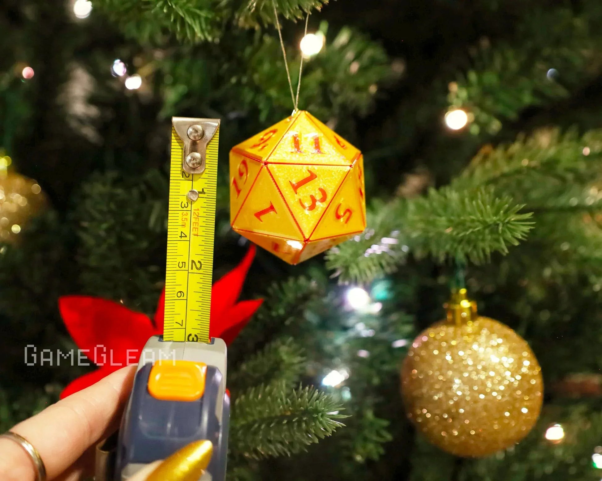 Yellow twenty-sided polyhedral dice ornament hanging on a Christmas tree, measured with tape.