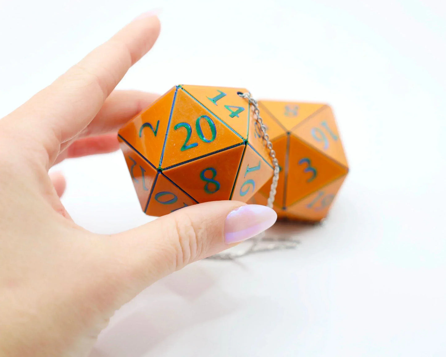 Hand holding orange twenty-sided dice charm with blue numbers and silver chain for car decor