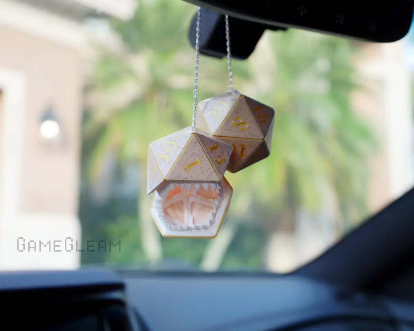 Holographic polyhedral dice car charm with monster mouth, hanging on rearview mirror.