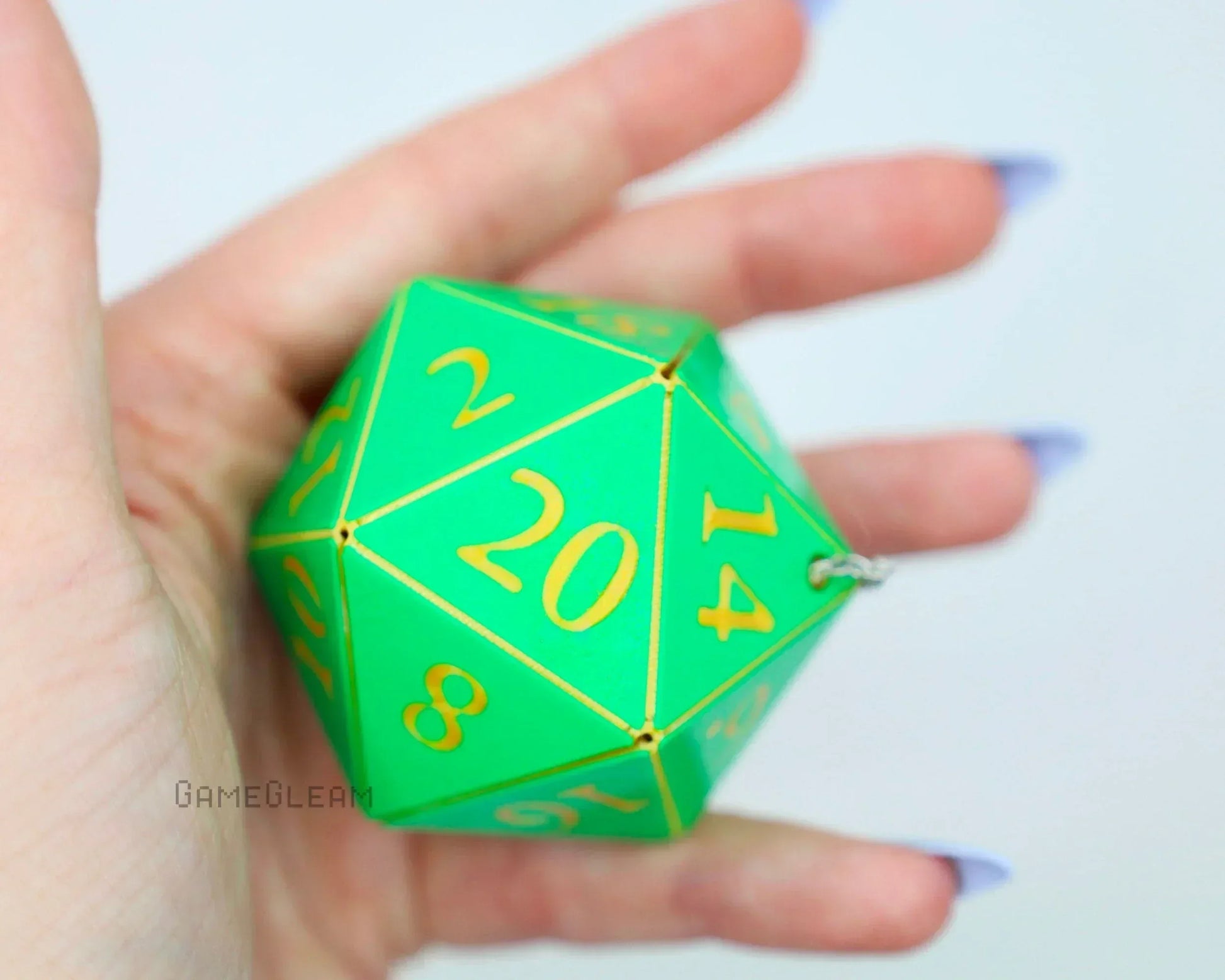 Hand holding green 20-sided dice charm with yellow numbers, car accessory for tabletop gamers