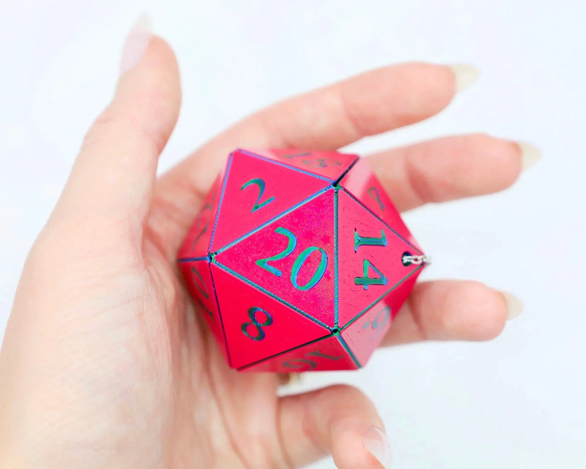 Hand holding a large pink twenty-sided dice with teal numbers, gamer accessory charm