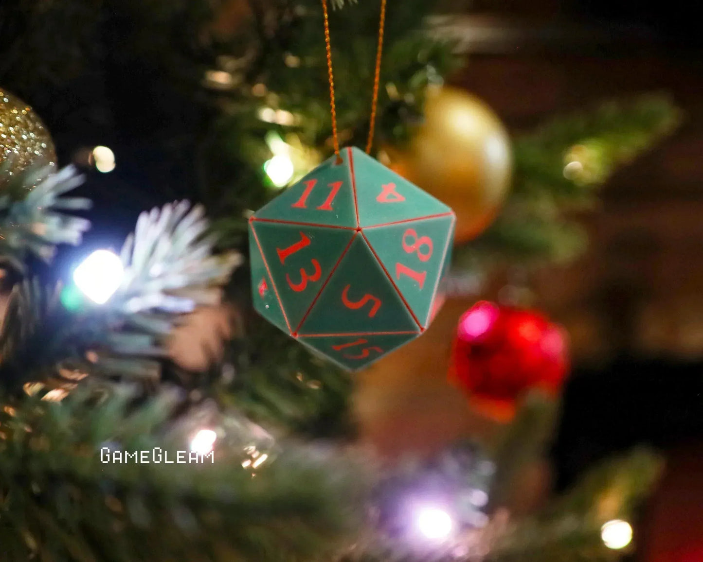 Green 20-sided dice ornament with red numbers hanging on Christmas tree with lights and baubles